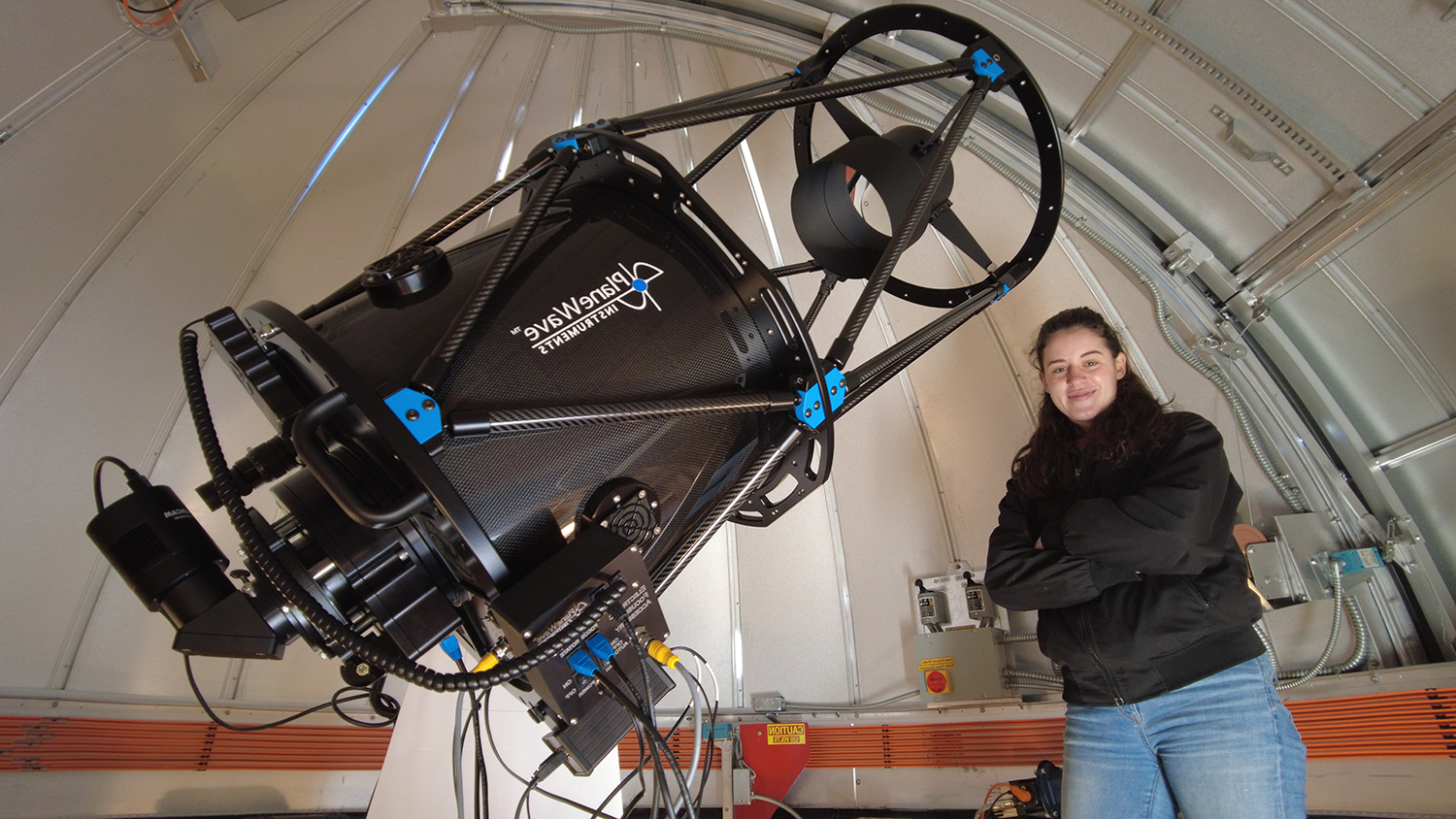 A photo of Rae Metrunec alongside the mounted telescope within the observatory. 