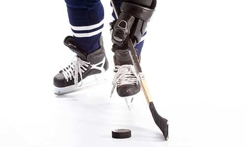 Knee-down shot of someone in hockey equipment standing on the ice while holding a stick, and a puck resting near the stick's blade.