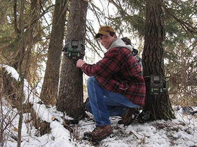 Photo of a student in winter, mounting research equipment on a tree