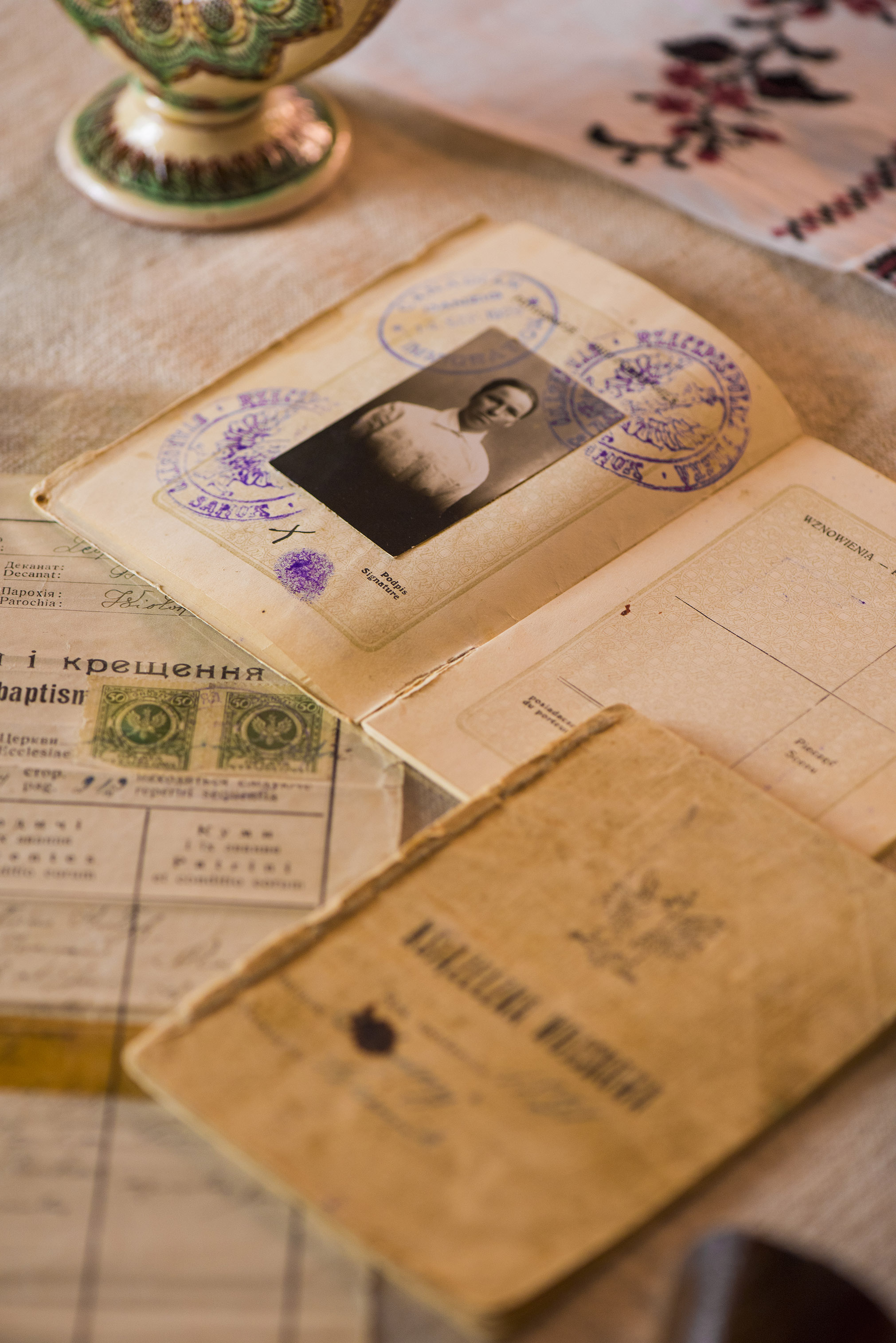 A small old passport-like book open to a page with a black and white photo of a woman surrounded by purple inked, circular stamps.