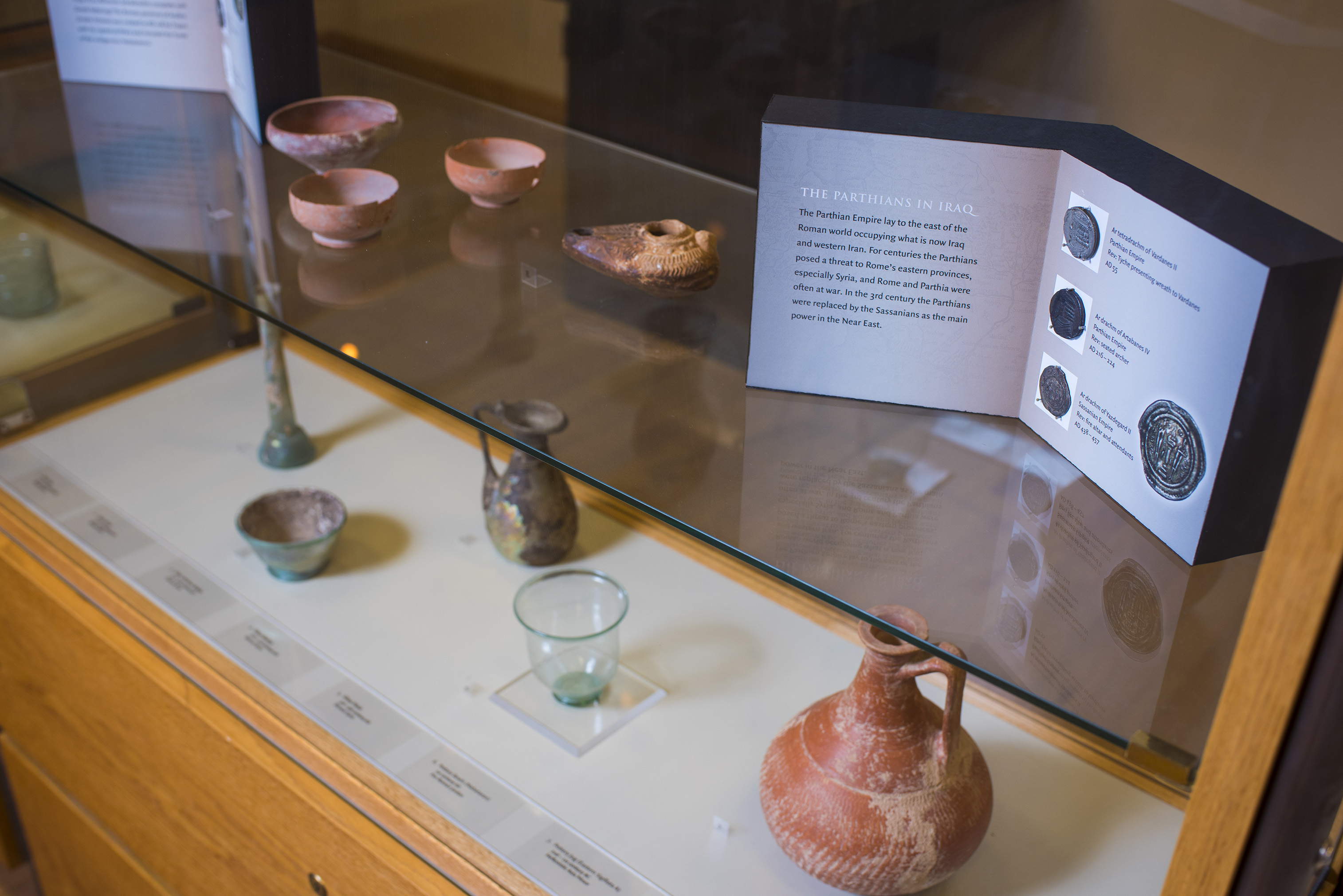 A glass display shelf displaying small clay dishes, amphorae vases, and small glass drinking vessels.