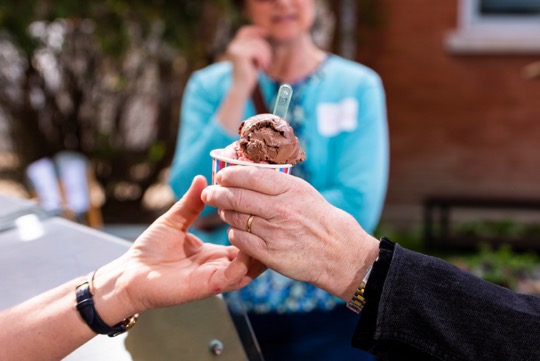 Two hands exchange a small cup of chocolate ice cream with a spoon.
