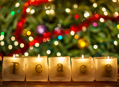 Letters that spell "peace" adorn small candles arranged in front of a close-up view of a decorated Christmas tree.