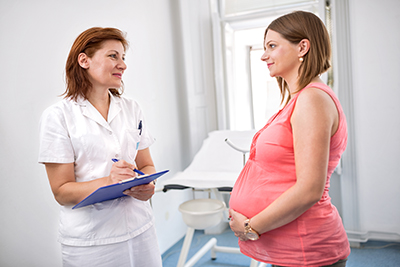 Thinkstock image, doctor with chart speaking to standing pregnant woman in examination room