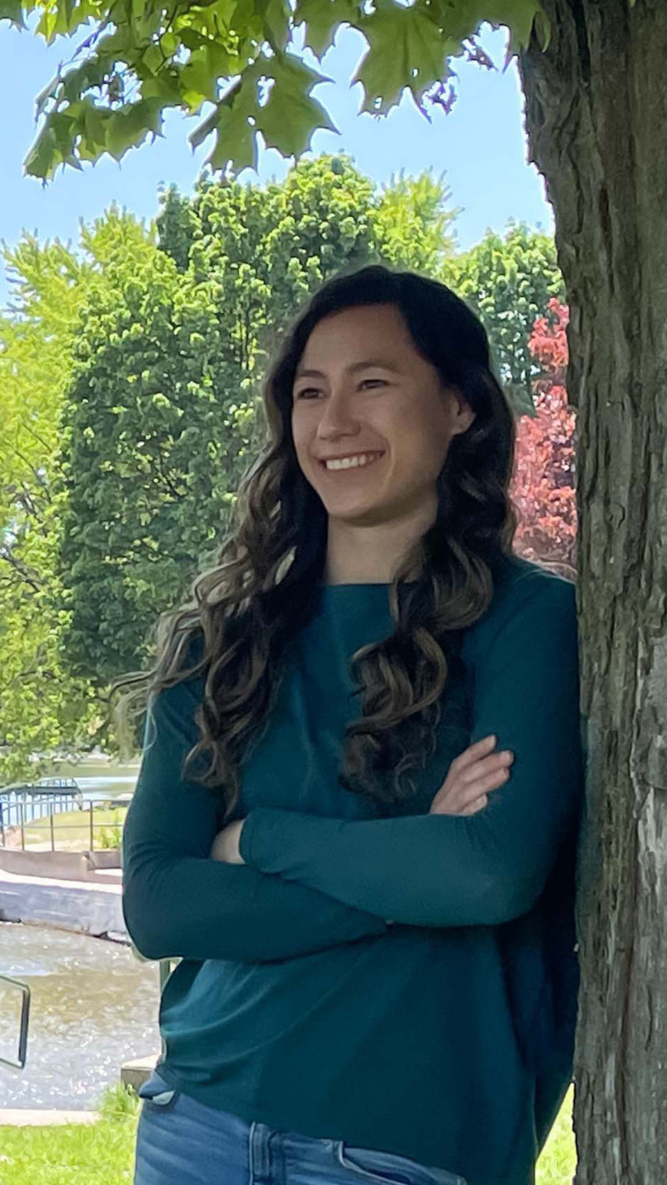 Meghan leans against a tree outside and smiles into the distance