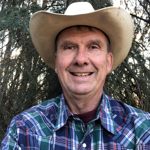 Rod poses outside wearing a cowboy hat and colorful plaid