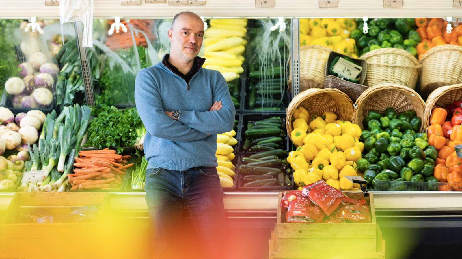 Man standing at a produce counter with vegatables behind him.