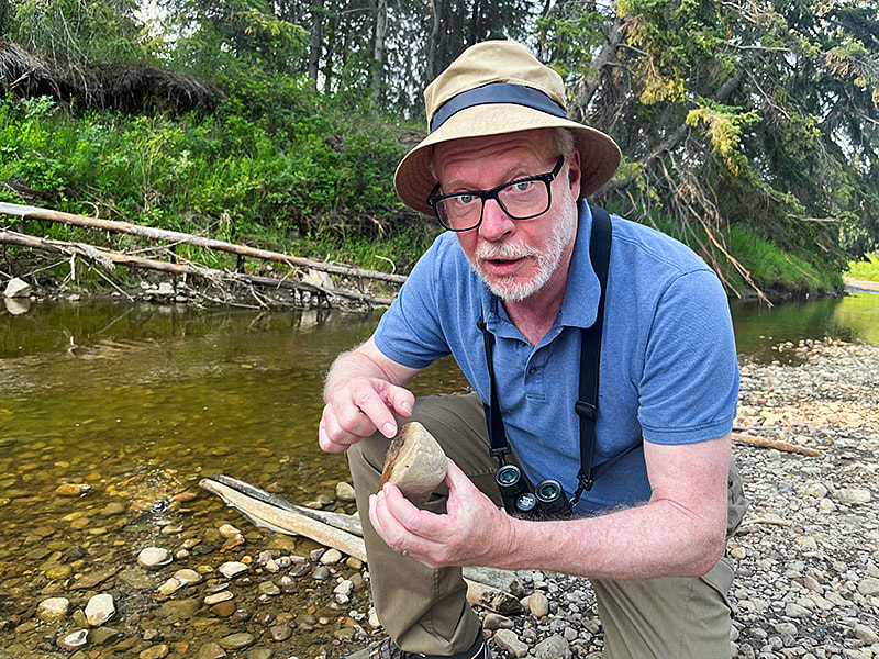 John Acorn holding and inspecting a rock in a creek bed.