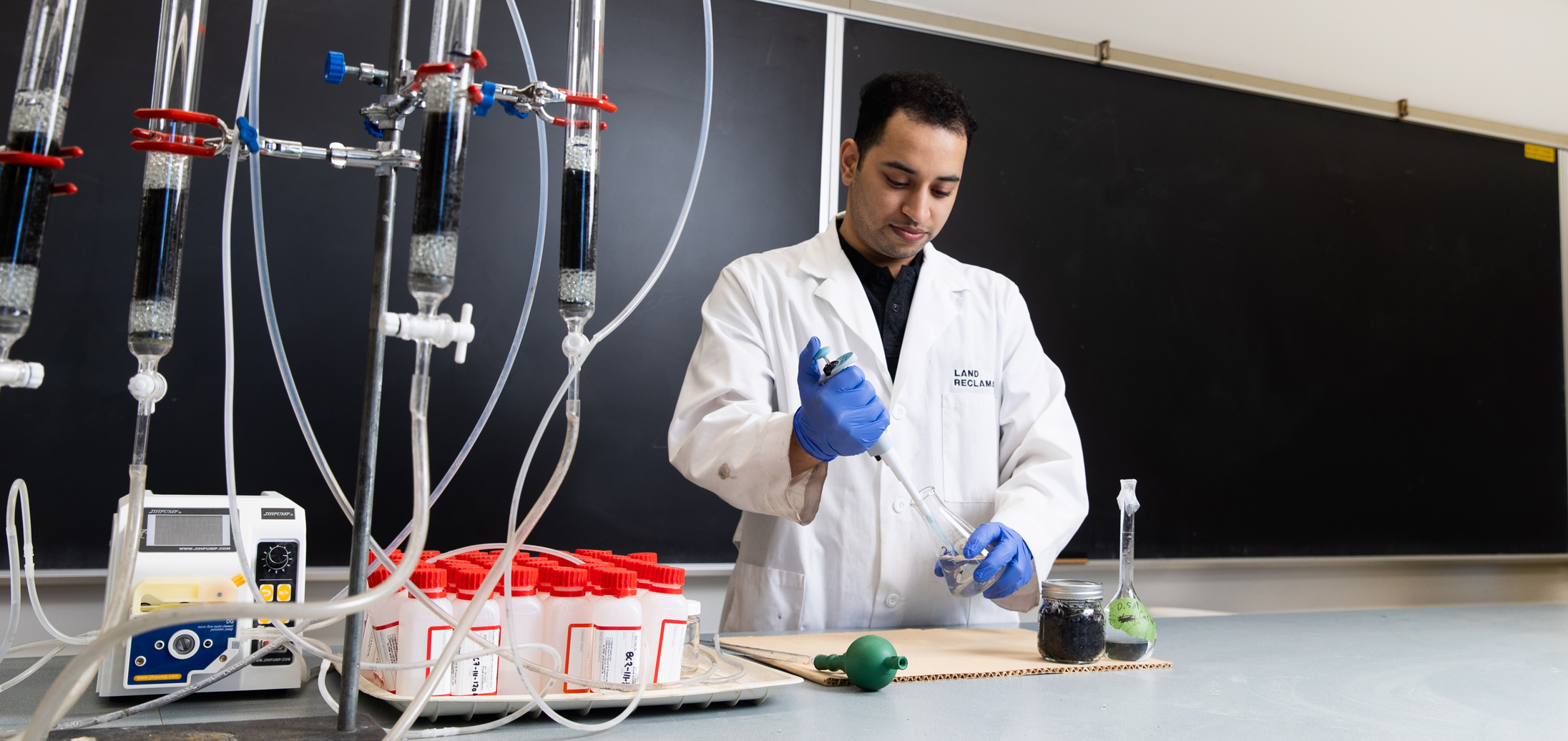 Researcher demonstrates pipetting biochar in front of a black chalkboard