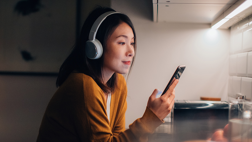 Young Woman With Bluetooth Headphones Listening To Music On Smartphone.