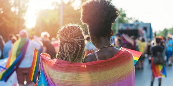 Two women shoulder to shoulder wrapped in pride flag