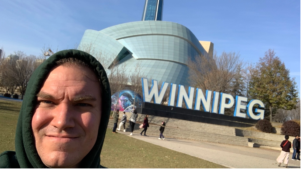 Author selfie in front of a sign that reads Winnipeg