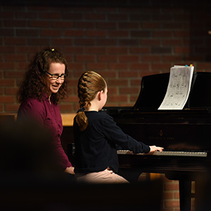 An instructor sitting at a piano watching her student play.