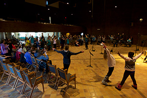 A group of people singing in a big circle with their arms up