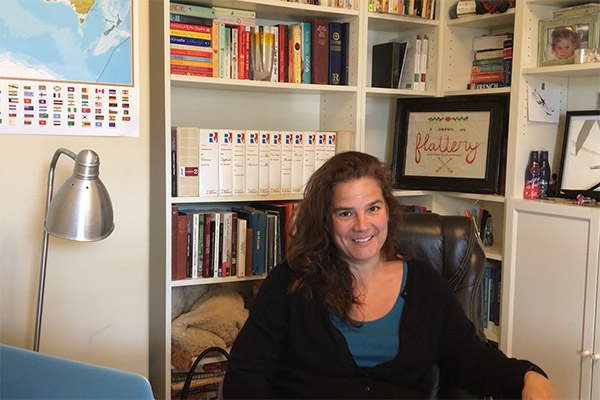 Professor Methot sits at her desk at home with a book case and map of the world in the background.