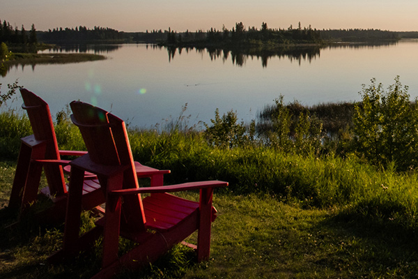 A promotional photo of two red wooden chairs set up in front of a lake and forest for the Get Outside Webinar series.