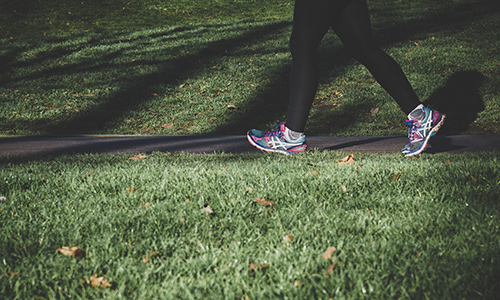 A person wearing bright running shoes is walking through a path surrounded by green grass on each side.