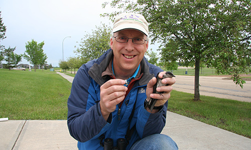 A photo of Glen Hvenegaard holding a small bird outside.