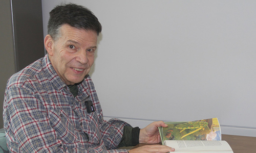 Photo of Paul "Sparky" Johnson sitting at a table with a book, looking sideways at the camera and smiling.