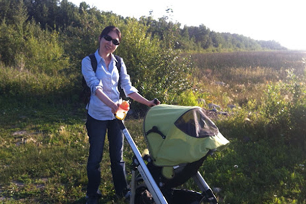 Photo of Mi-Young standing in a grassy area, wearing sunglasses and standing beside a stroller.