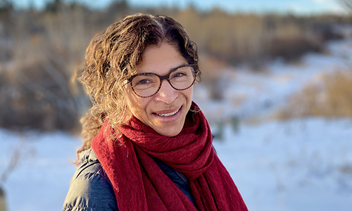Photo of Tammy Richard in a red scarf and glasses, hair pulled back, in a snowy backdrop as she smiles at the camera.
