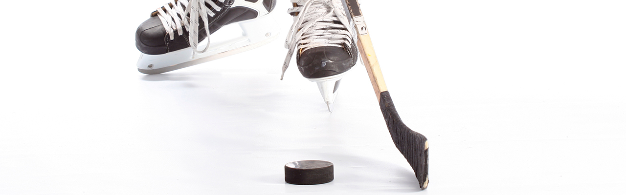 Someone in hockey skates standing on an ice surface with their stick and a puck resting on the ice.