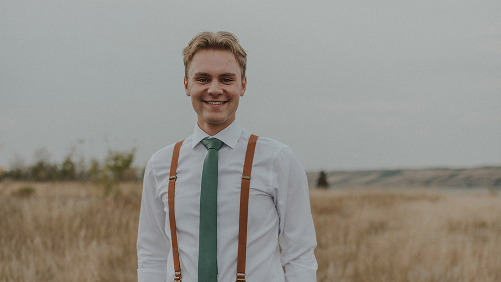 Portrait of student, waist up, smartly dressed standing in a field.