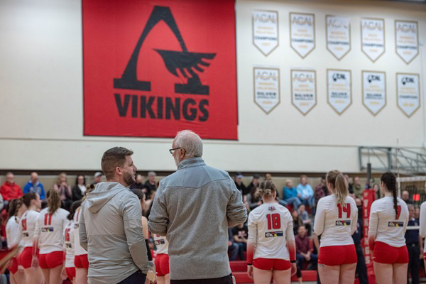 Steve Enright and assistant coach Bryan Laskosky taking as the Vikings women's volleyball team lines up on the court.