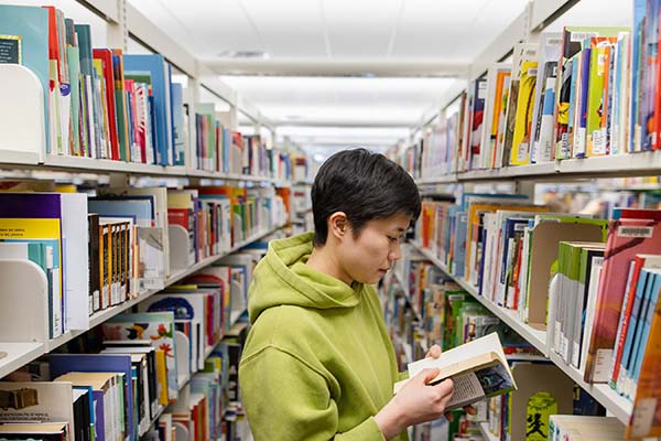 Student reading a book between bookshelves in a library