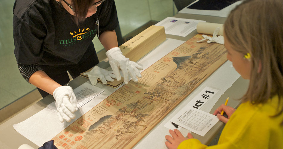 A photo of a child and museum employee looking at a scroll from Asia