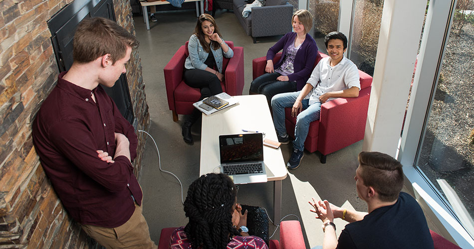 A photo of a group of students surrounding a table and laptop