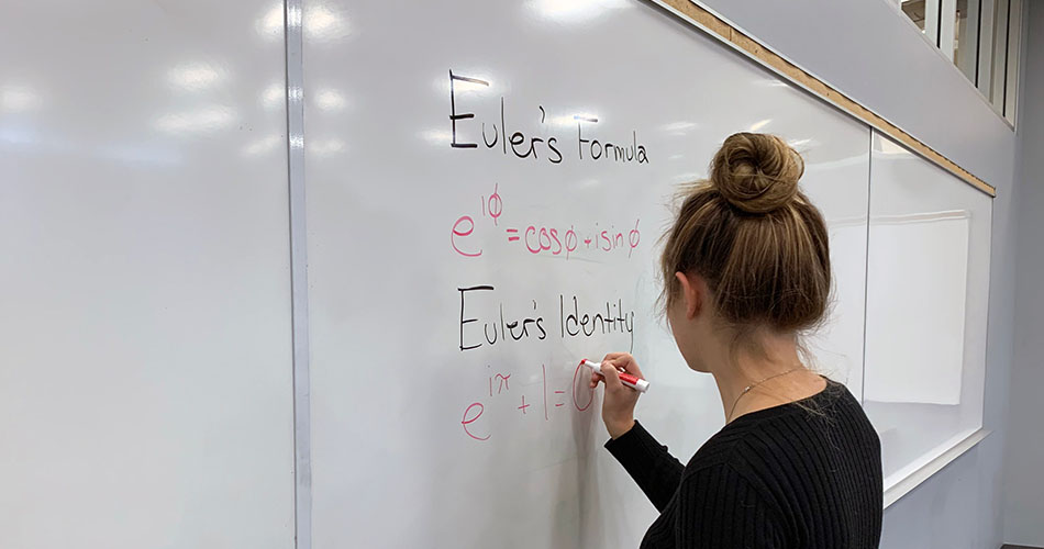 A photo of a student writing mathematical formulas on a whiteboard