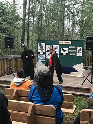 A presentation on a stage in the woods with 2 actors dressed up in costumes.