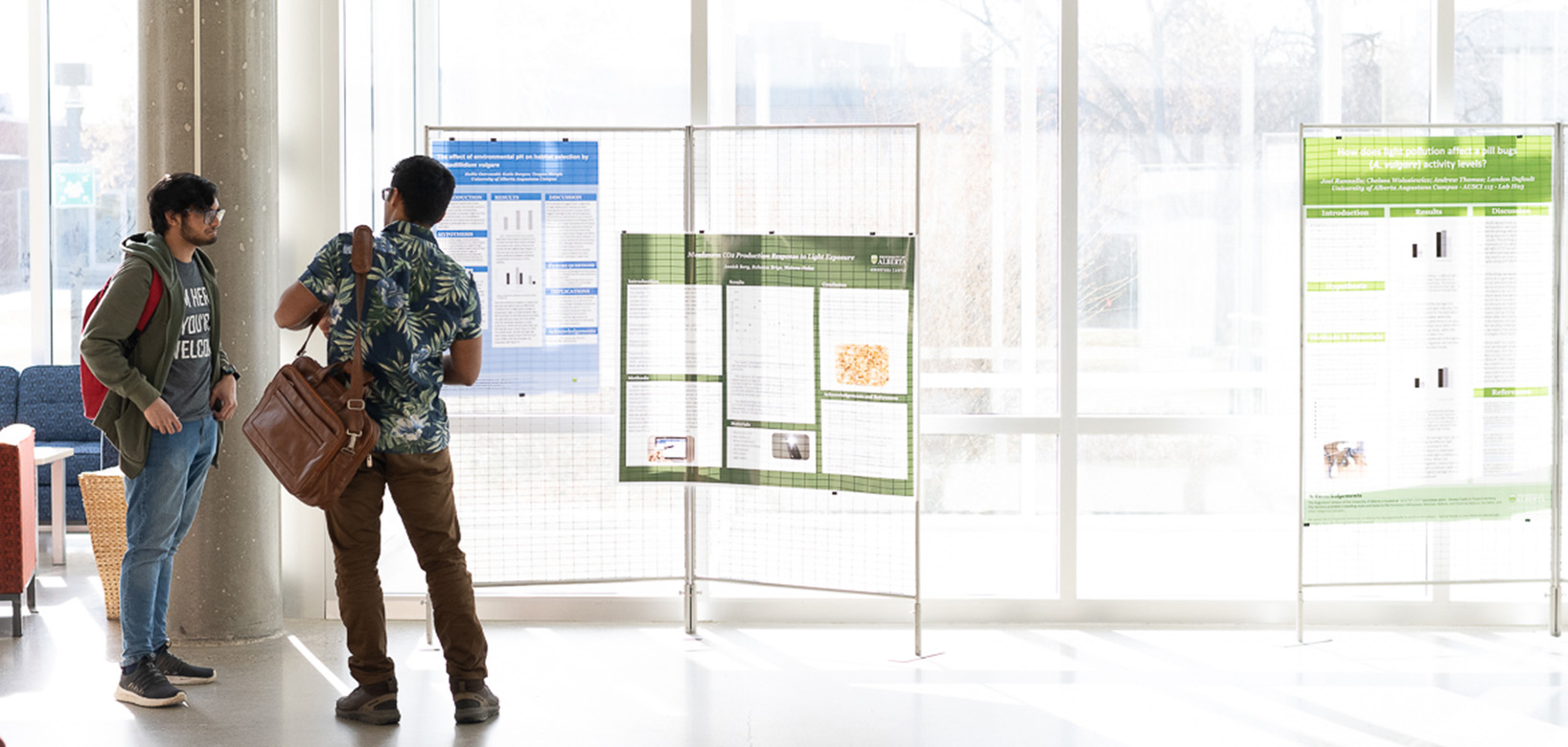 Two students standing in an open, brightly lit building in front of display panels that have research posters on them.