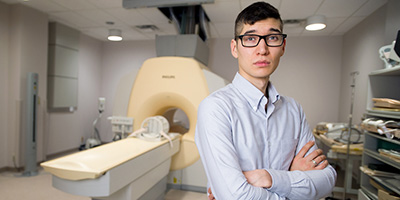 Photo of Dylan Breitkreutz standing in front of an MRI machine.
