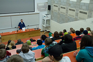 A room full of kids watching a chemist conduct interesting demonstrations at the front of the room