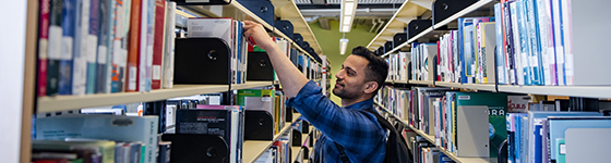 A student selecting a book from a shelf in the library.