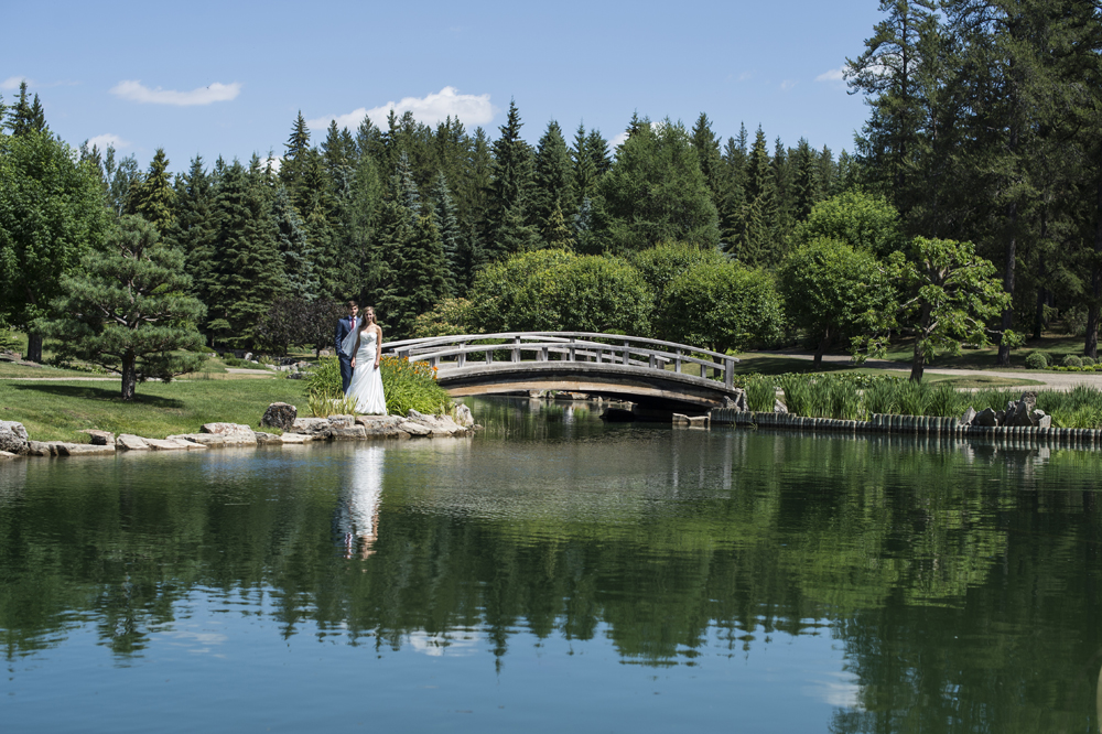 Bride and groom standing in front of the curved wooden bridge in Kurimoto Japanese Garden