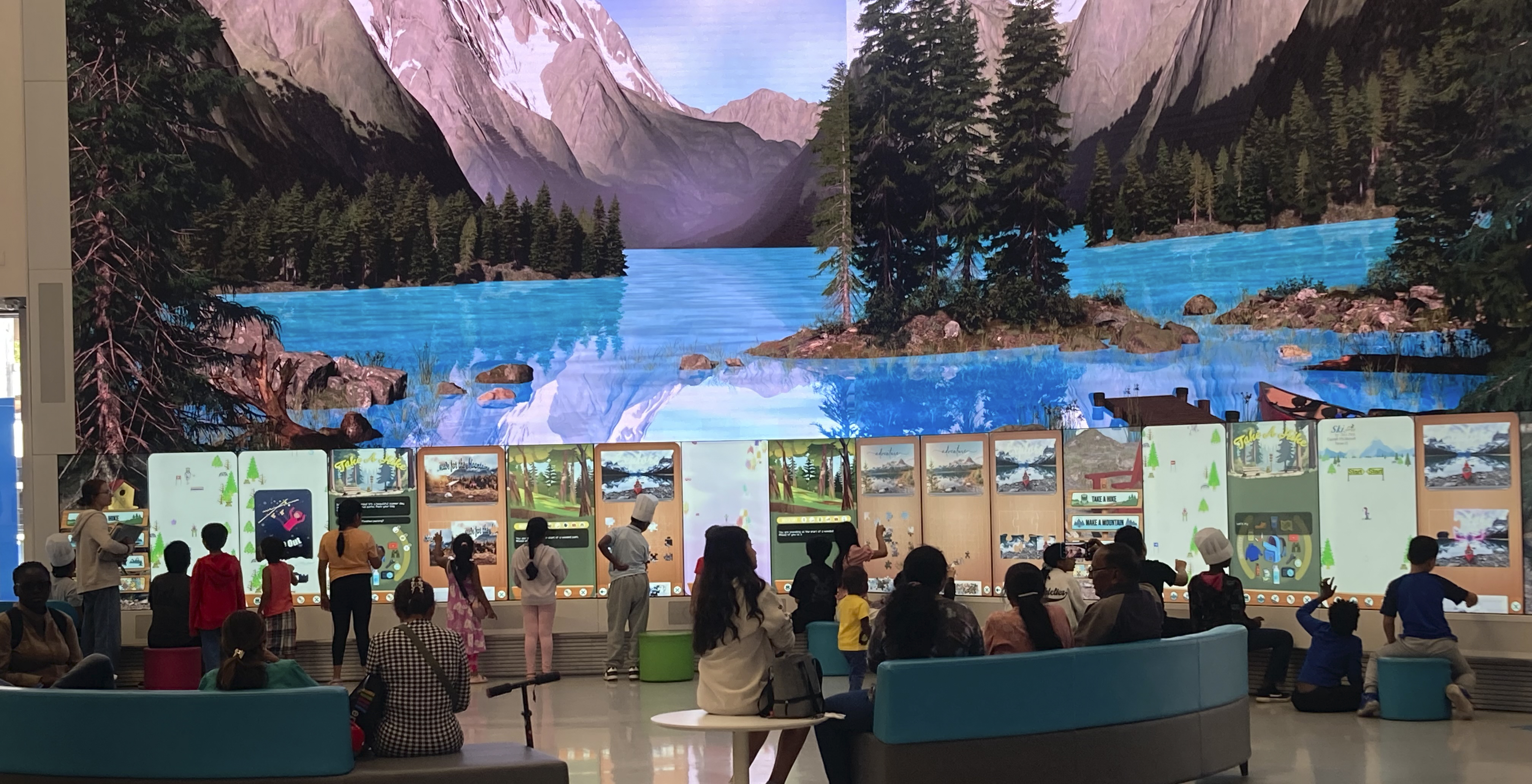 Kids playing multiple interactive games on a large screen with a mountain lake scene in the background.