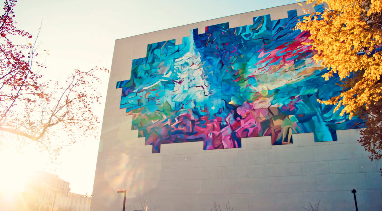 Exterior shot of the Education North building including a mural and autumn trees