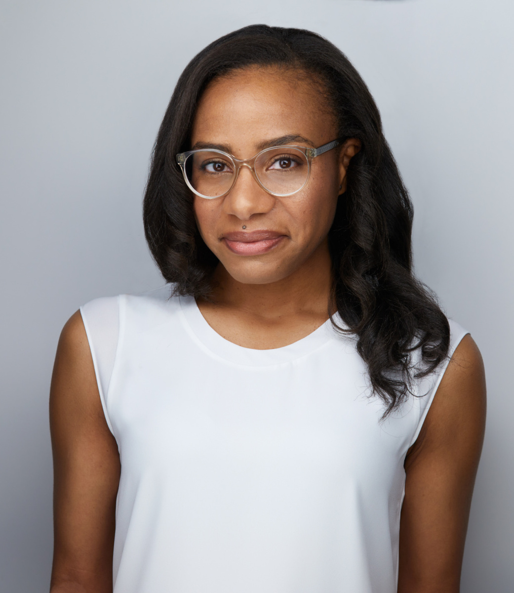 Portrait of Giselle Thompson - a Black-Caribbean woman with glasses and curled hair that falls just past her shoulders