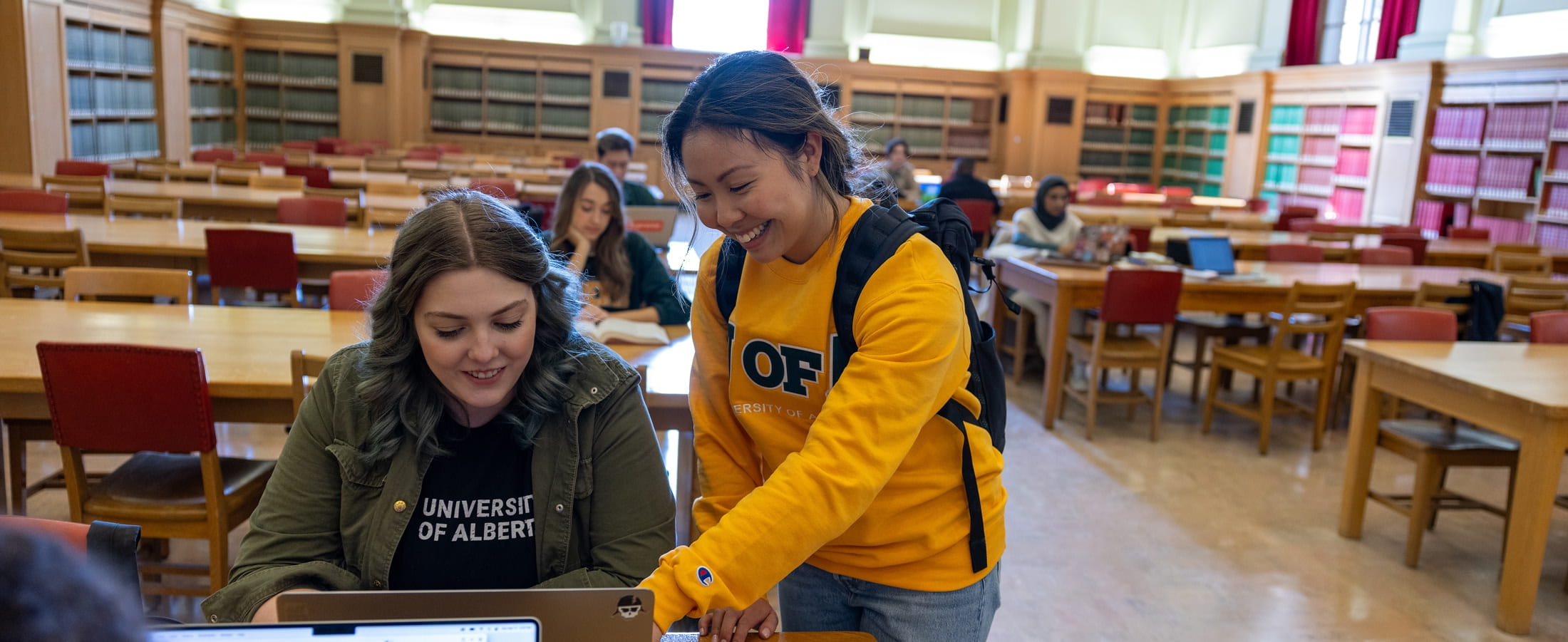 Two female students in a library looking at a laptop