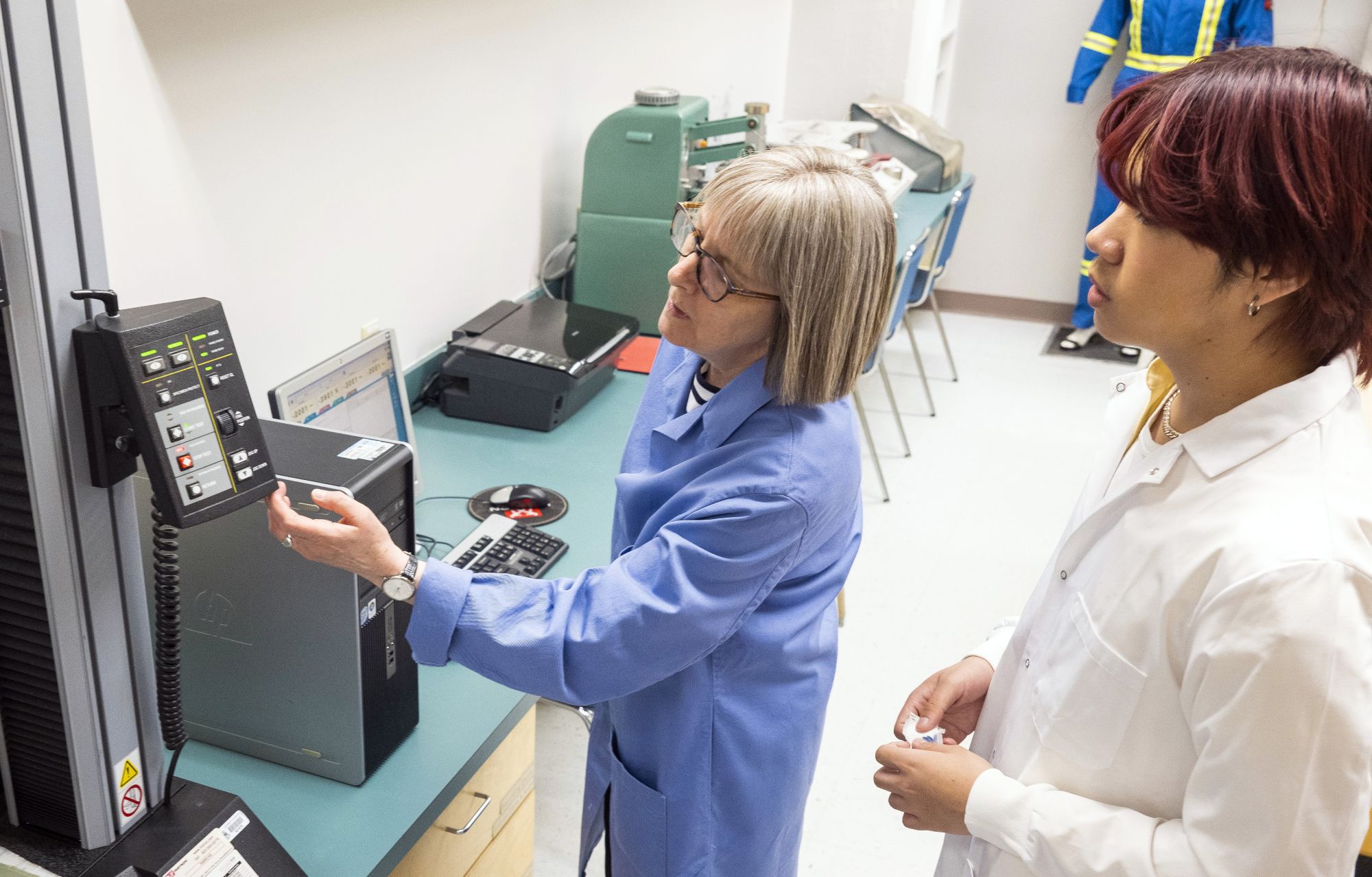 Instructor adjusting settings on a machine with a student watching, both in labcoats