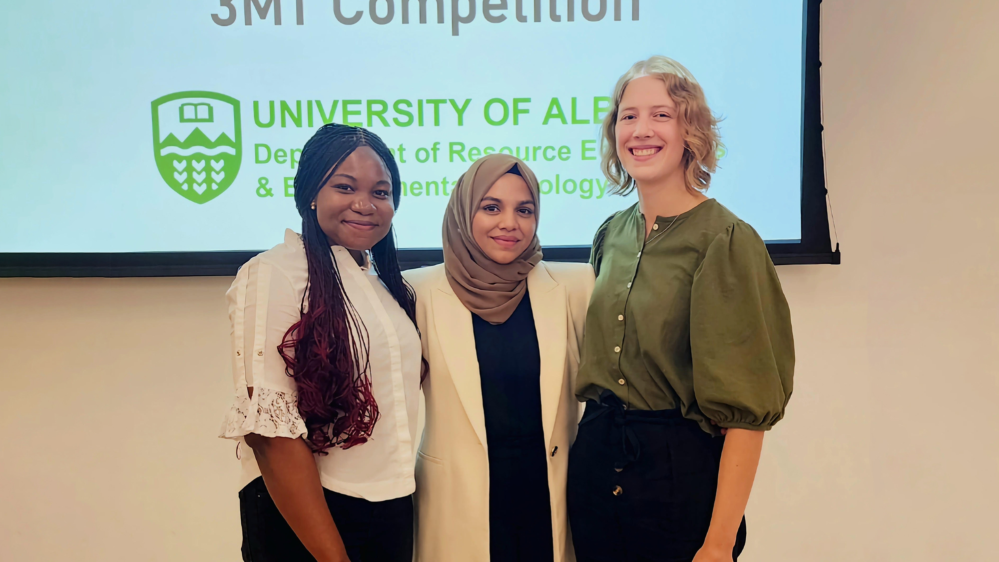 Three students dressed professionally pose at the front of a presentation room