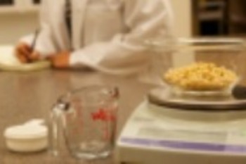 A counter with a bowl of pasta on a scale and a person making notes