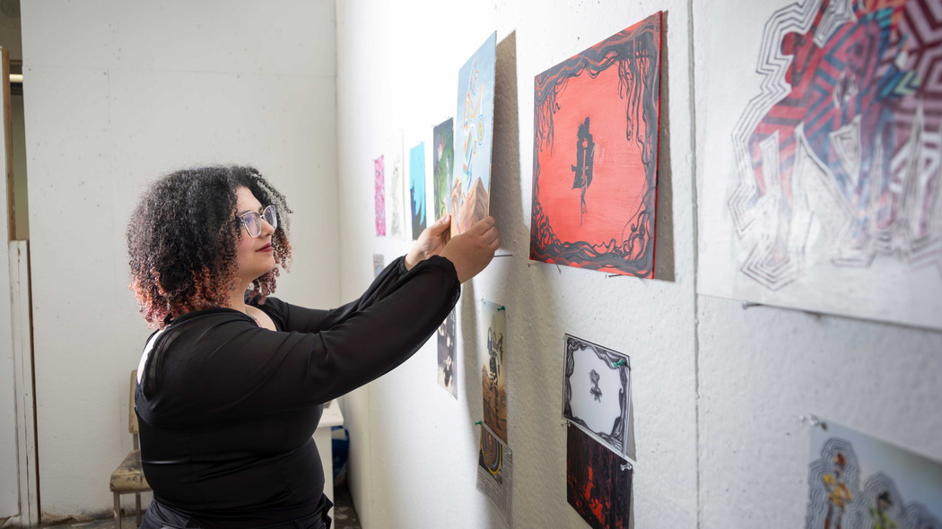 A student places artwork onto a wall amidst others in a gallery.