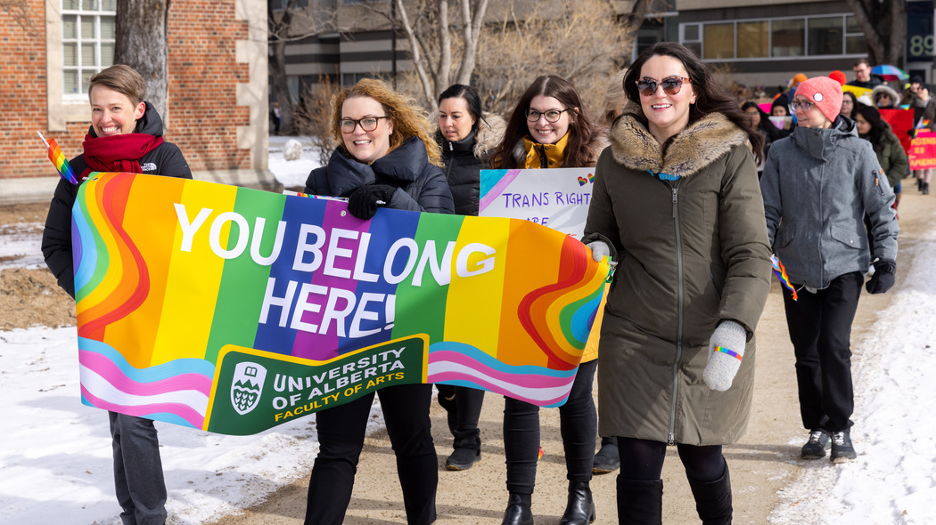 Campus students holding a "You belong here" rainbow flag walk in a campus Pride Parade.