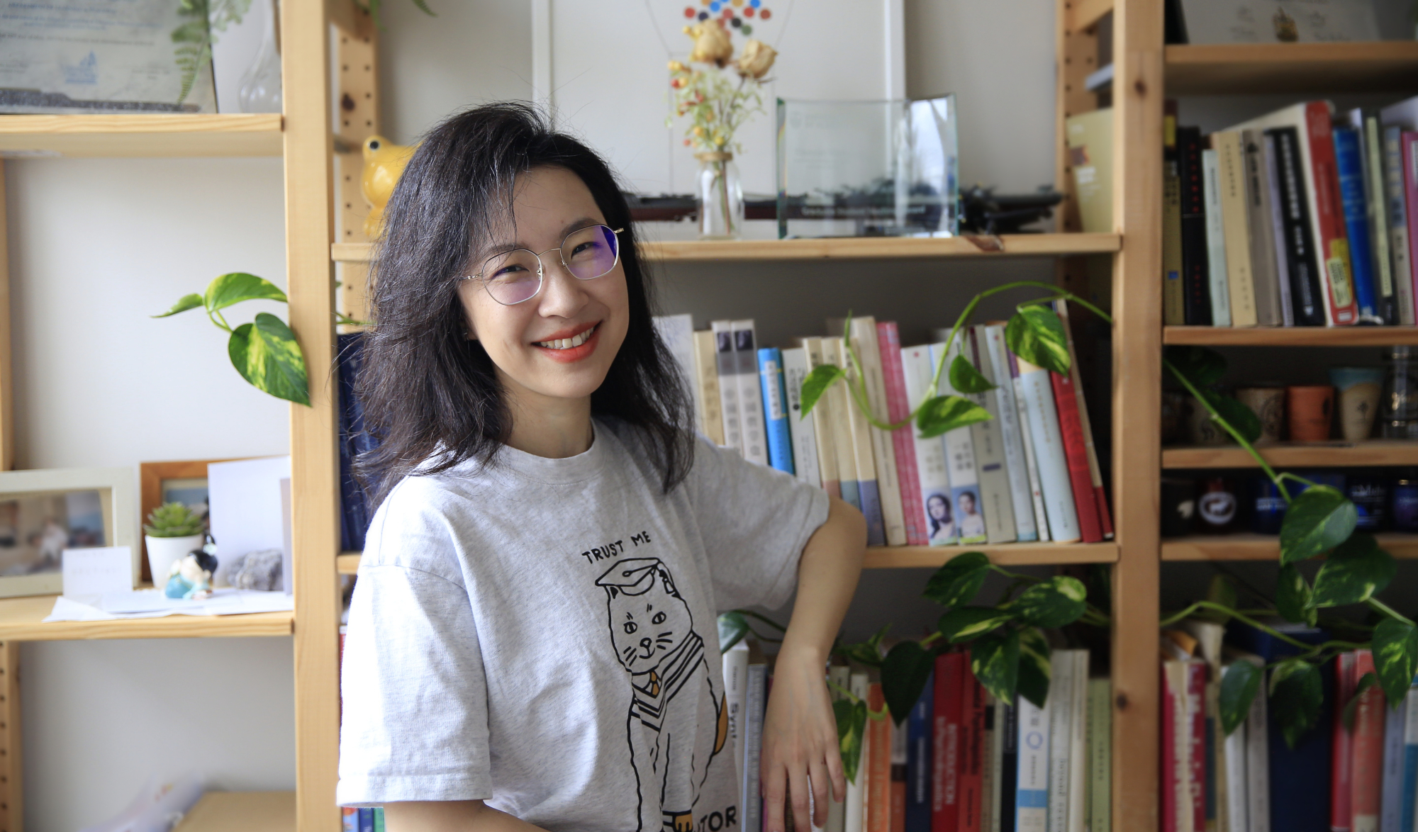An image of Dr. Xiaoyun Wang, a woman wearing a white t-shirt and standing in front of a bookcase.
