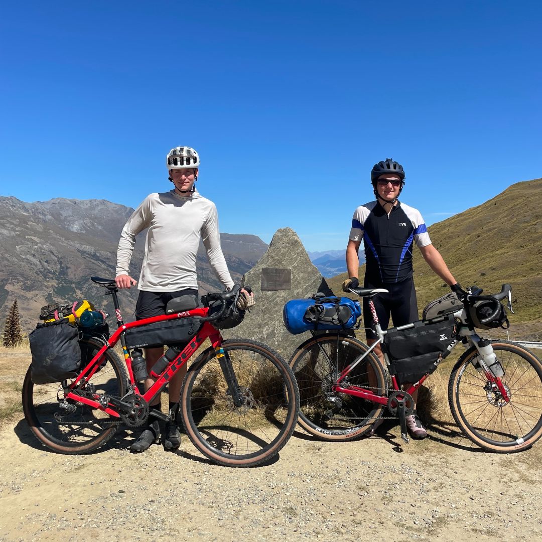 Luke Talman and Olivier Haley on a bikepacking trip across New Zealand, pictured on a mountain top with helmets and their bikes