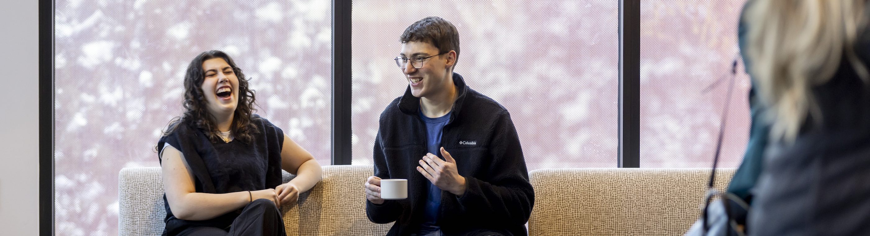 Two alumni laugh on a couch at an Alumni event